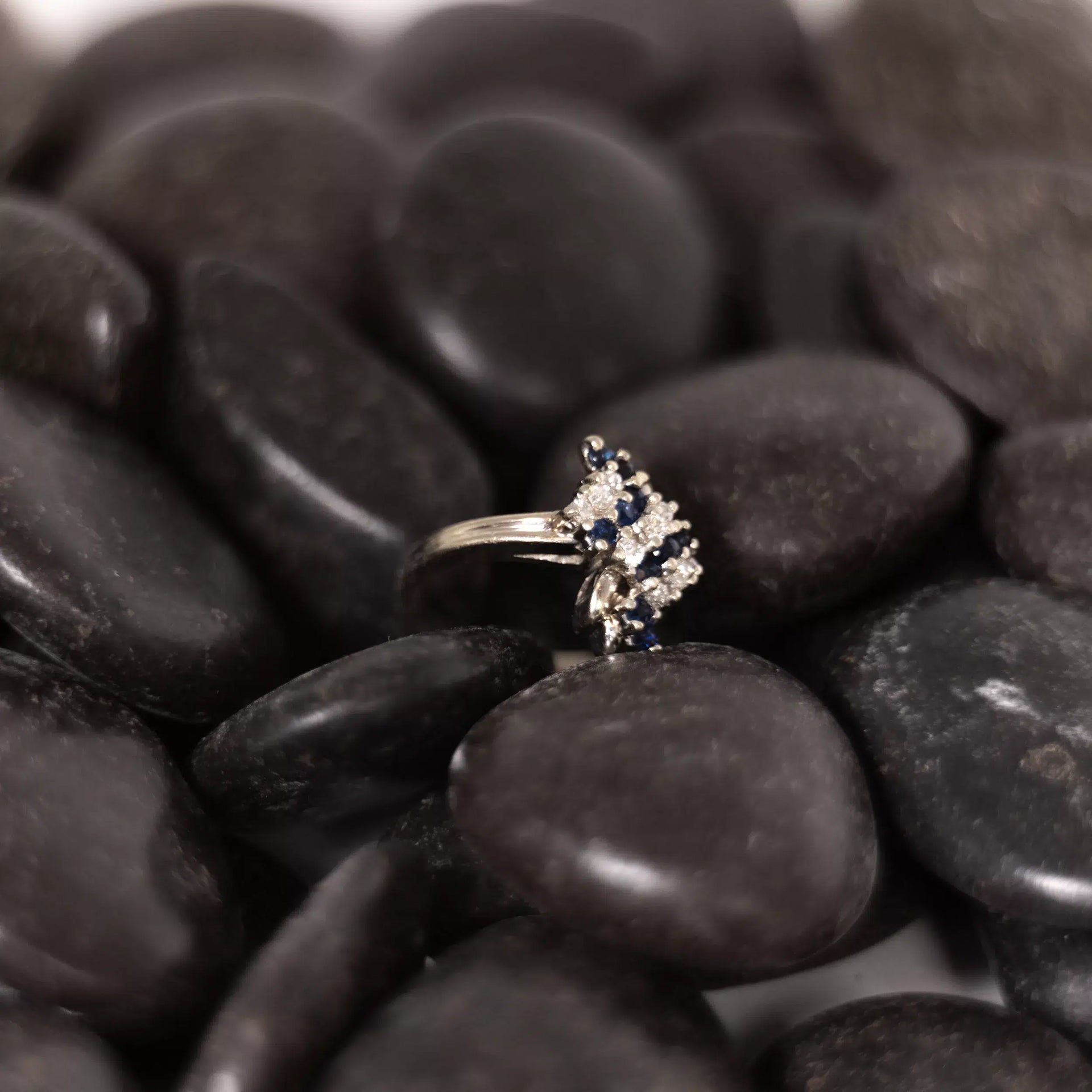 A sapphire and diamond ring sitting on a pile of rocks, accentuated by the shimmering 14 Karat Yellow Gold Fashion Chain.