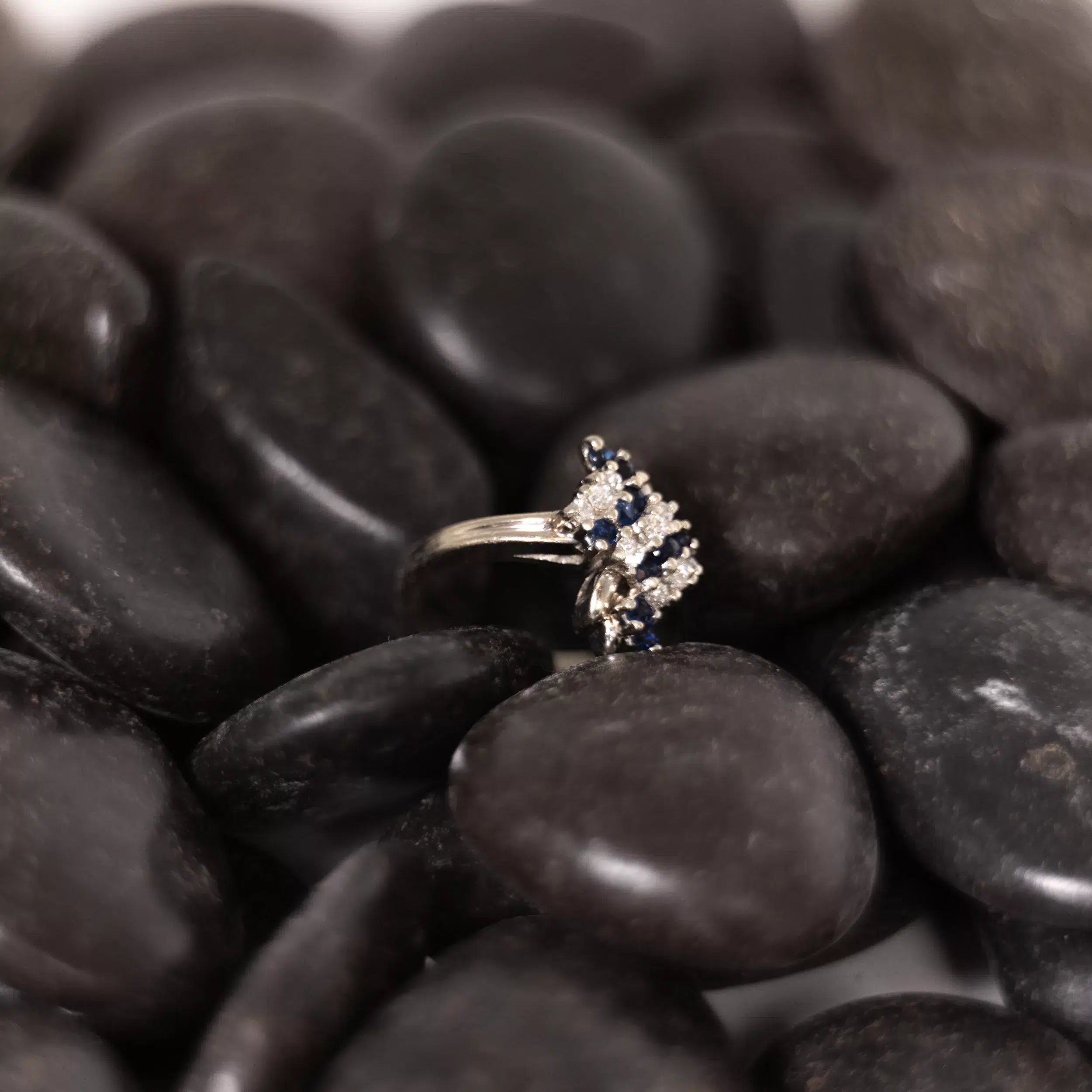 A sapphire and diamond ring sitting on a pile of rocks, accentuated by the shimmering 14 Karat Yellow Gold Fashion Chain.